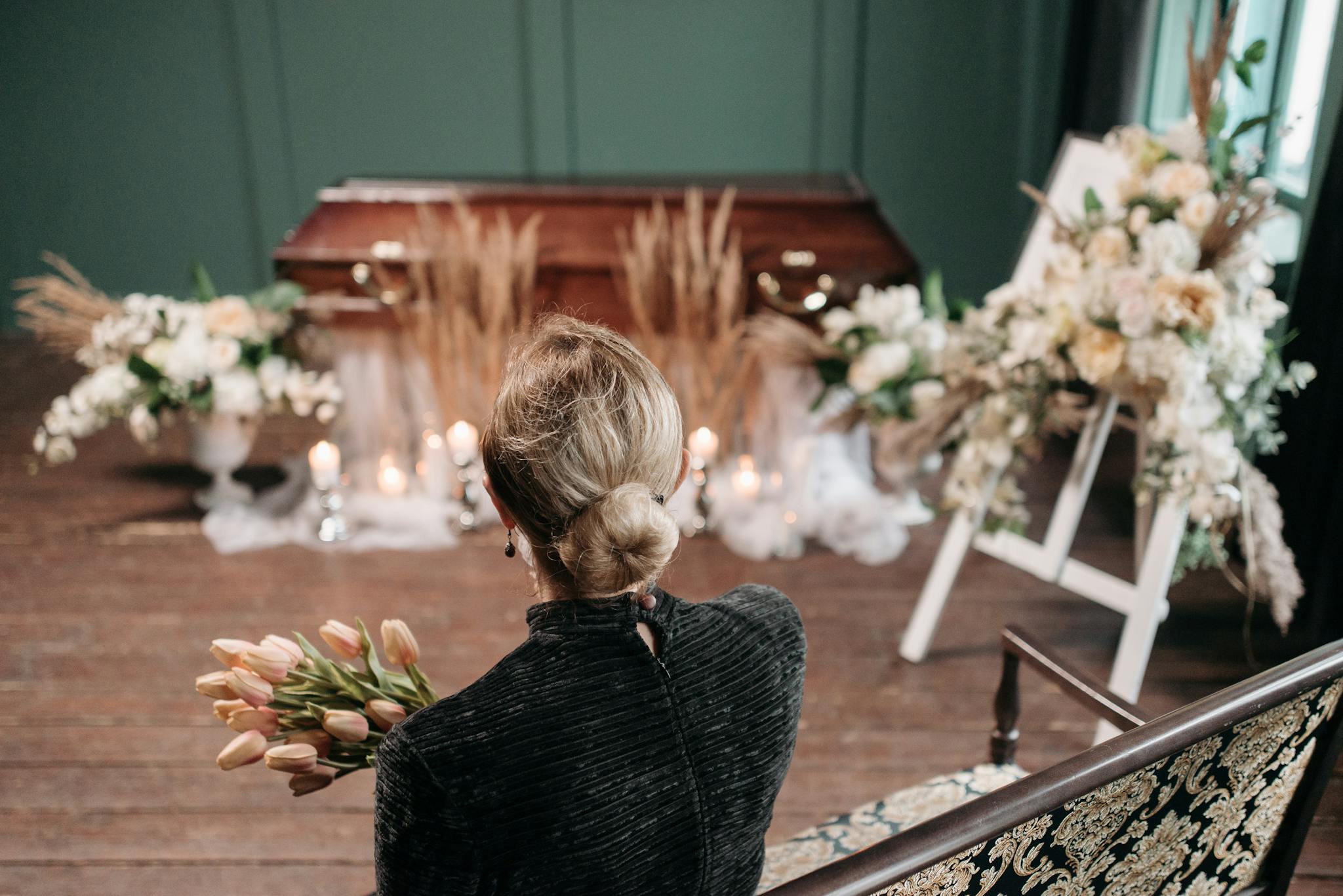 A woman mourns at an indoor funeral ceremony with floral decorations and a coffin.